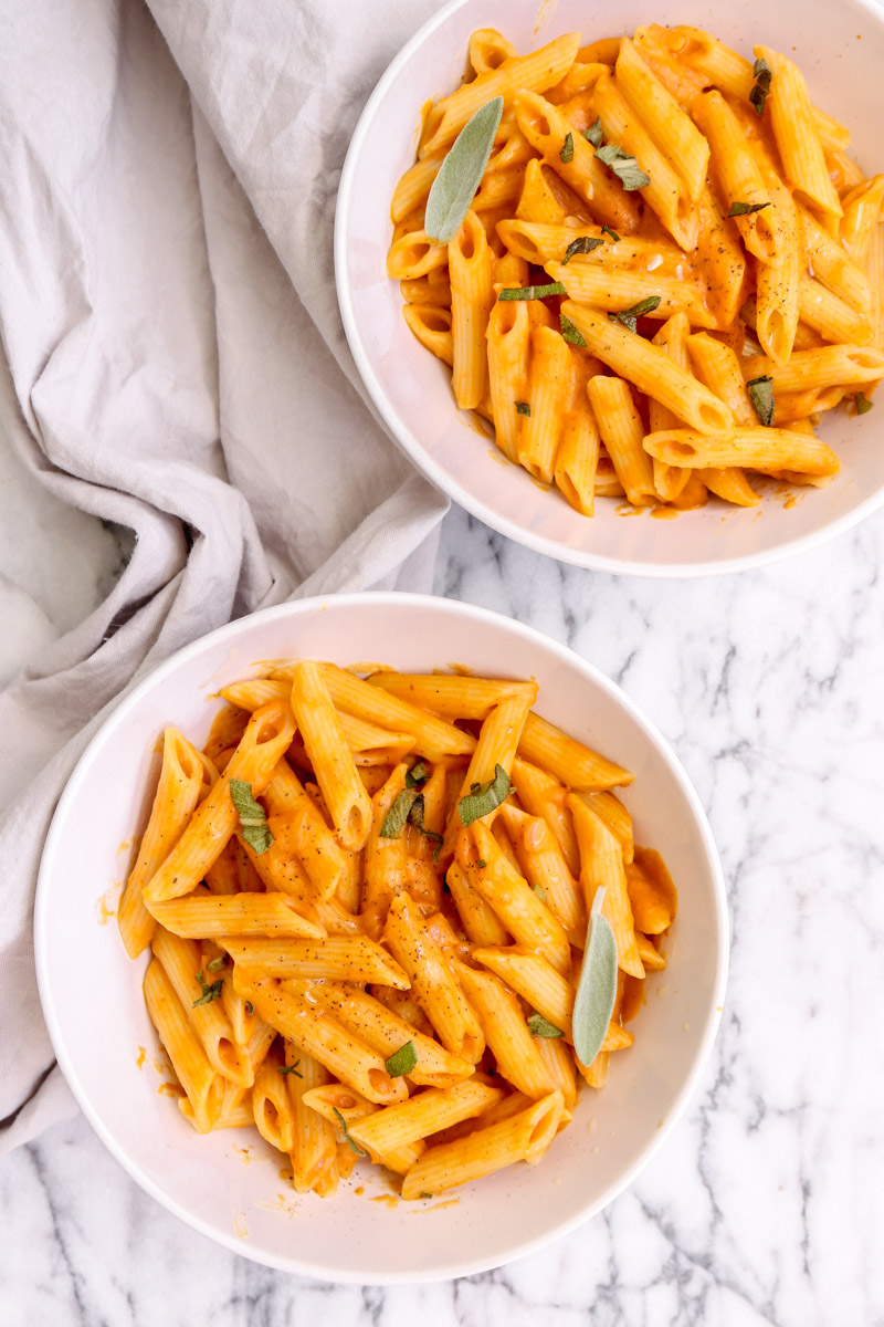overhead image of vegan pumpkin pasta in white bowls.