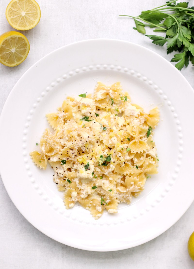 overhead image of pasta on a white plate and lemons in background