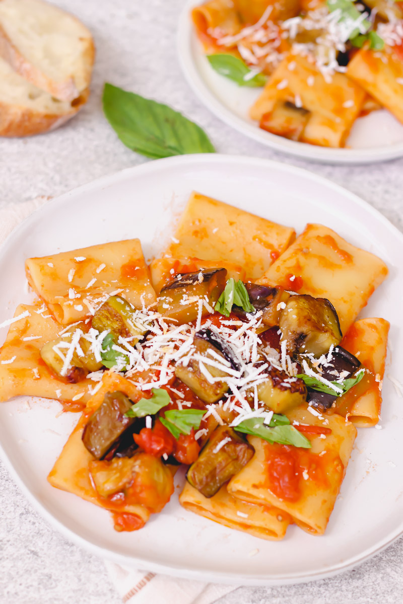 close up image of pasta alla norma on a white plate and bread in background.