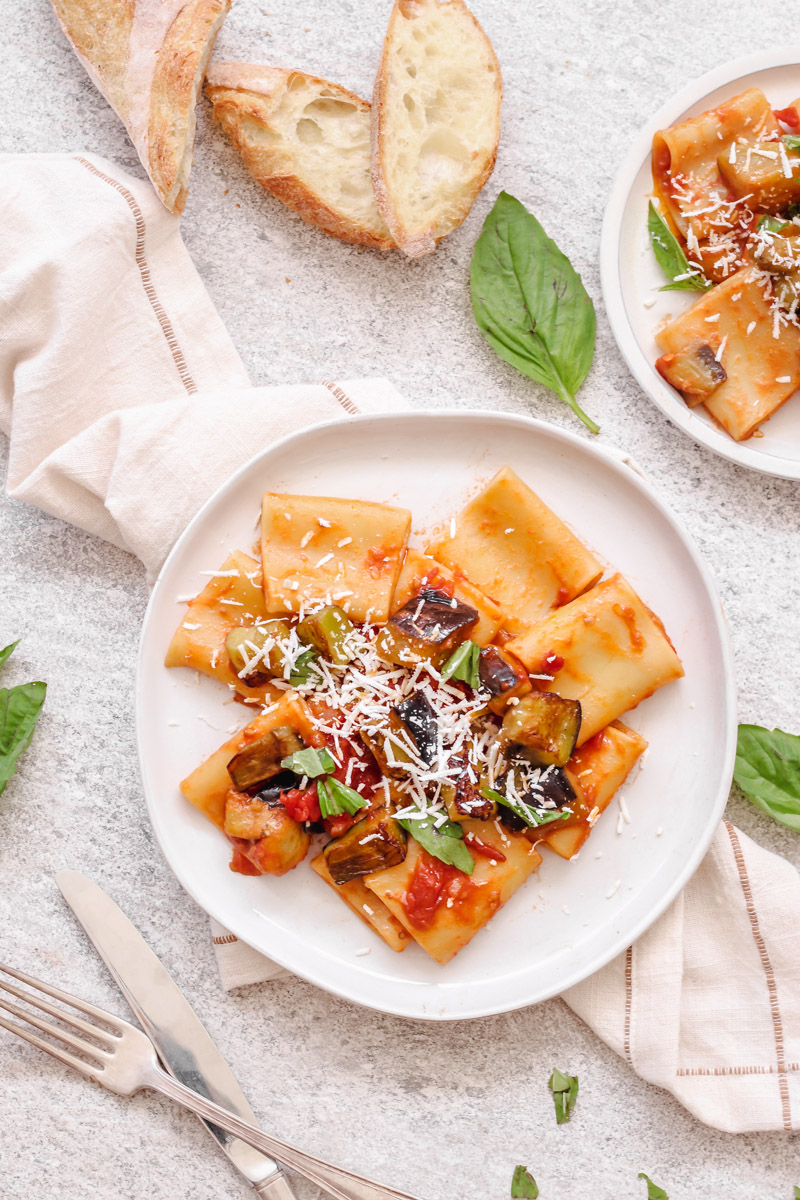 overhead image of pasta alla norma on white plate and bread in background.