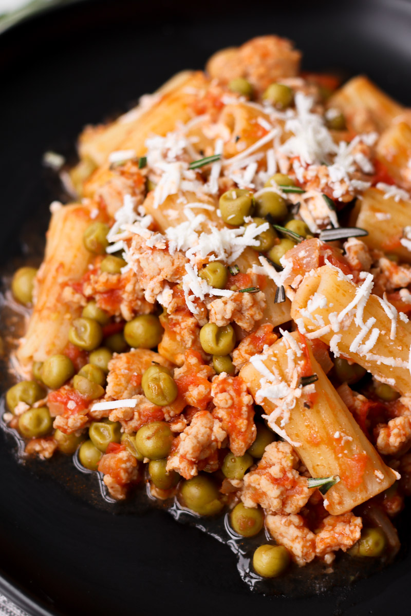 overhead image of pasta with ground chicken and peas on a black plate