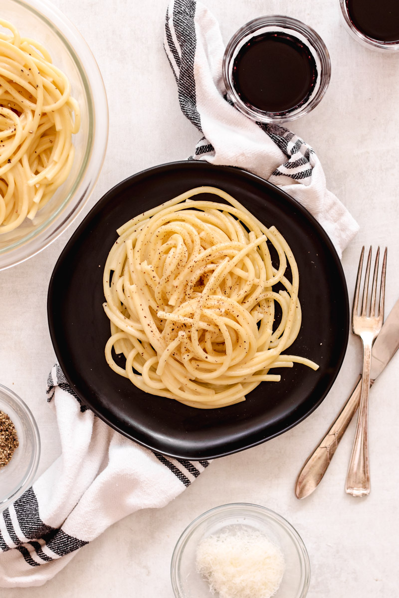 overhead image of pasta on a black plate and cups of a dark drink. 
