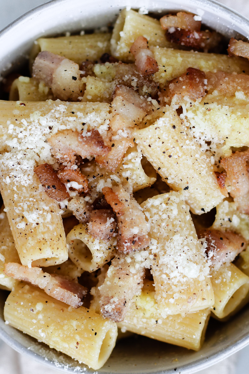 close up image of pasta with grated cheese and black pepper flakes. 