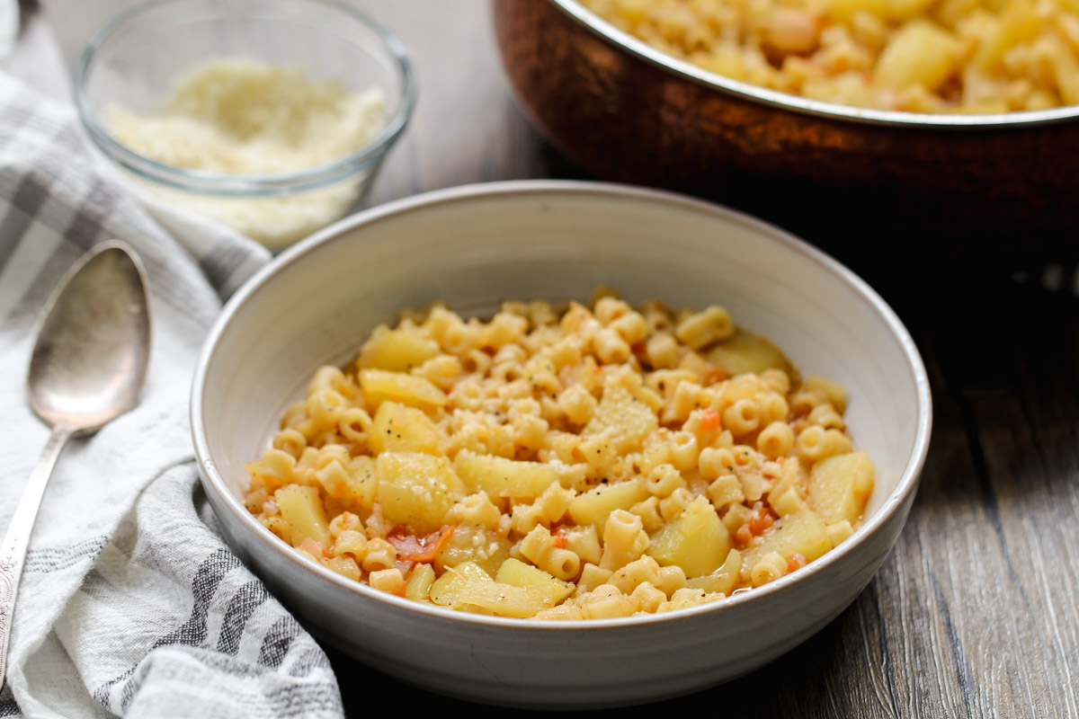 close up image of pasta and potatoes in a small bowl with a towel with a spoon. 