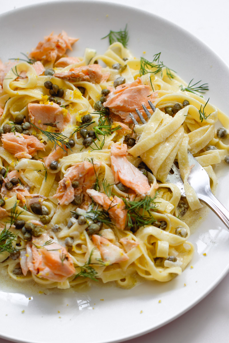 close up image of creamy salmon pasta on white plate with a fork around the pasta.