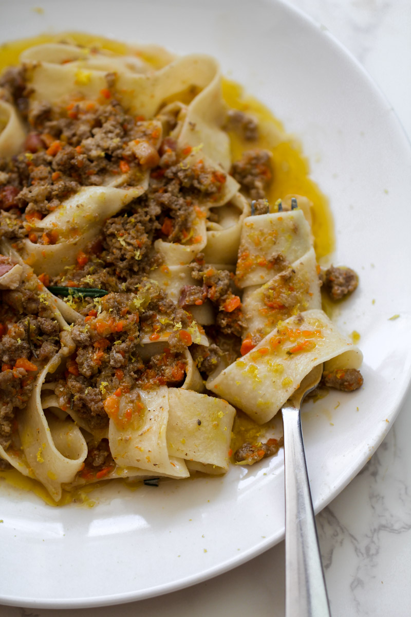 close up image of a pasta with a white ragu on a white plate and a fork. 