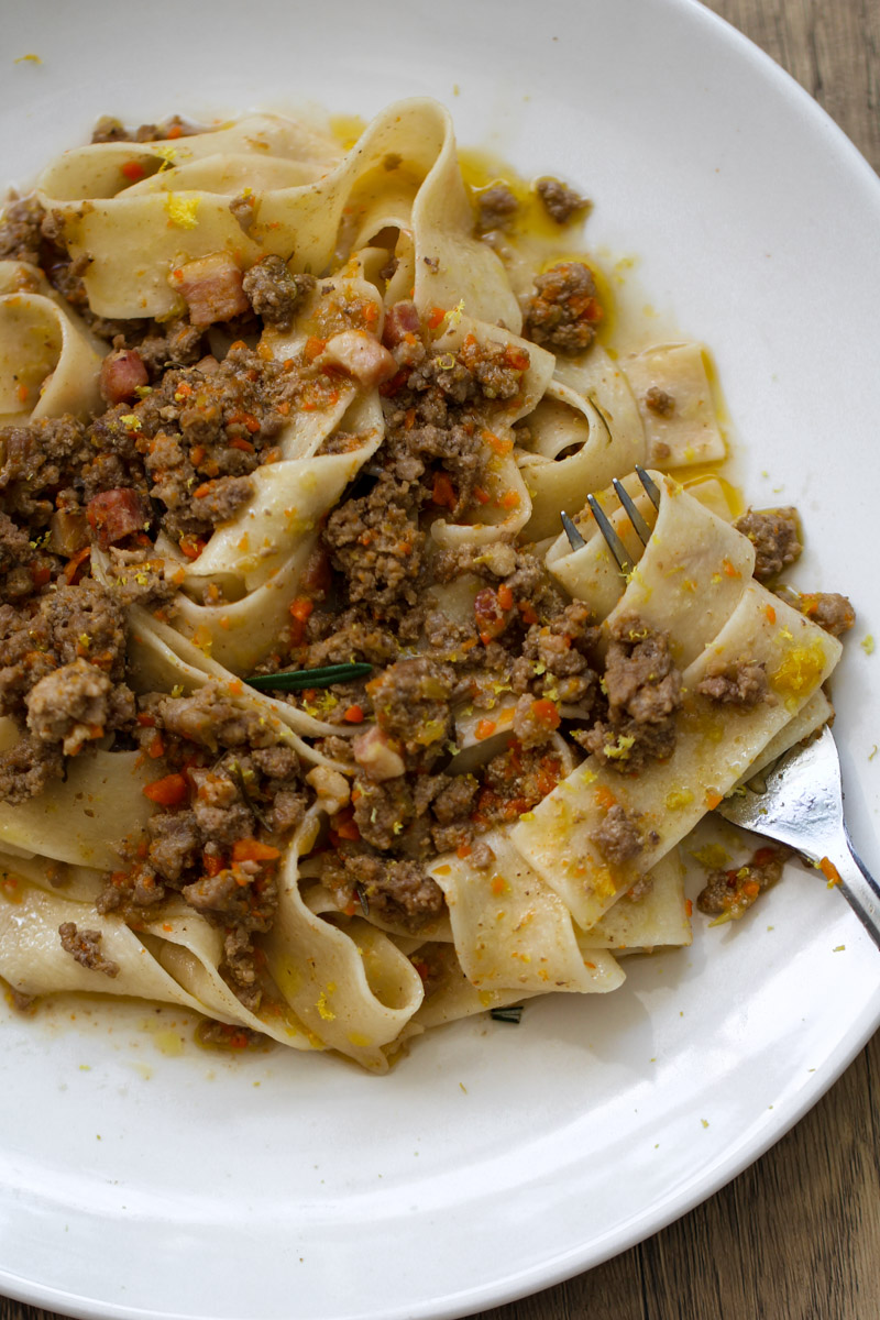 Close up image of a white ragu sauce with pasta on a white plate. anda fork. 