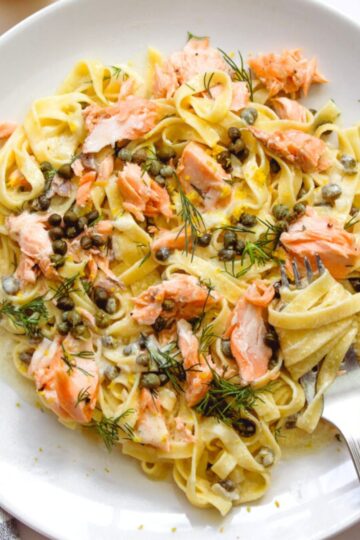 Creamy salmon pasta with lemon and parsley on a white plate.
