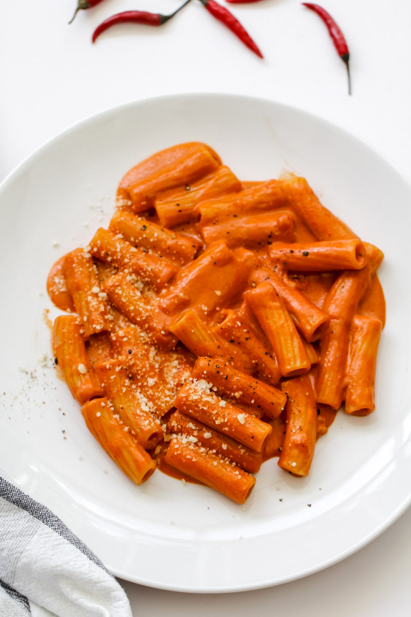 close up image of creamy tomato pasta on a white plate with Parmigiano Reggiano. 