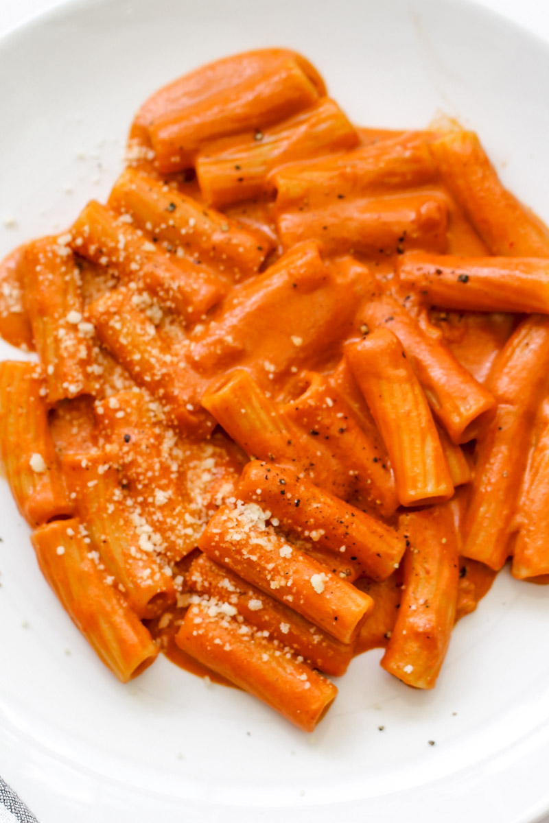 close up imgae of Italian creamy tomato pasta recipe plated on a white plate with Parmigiano cheese.