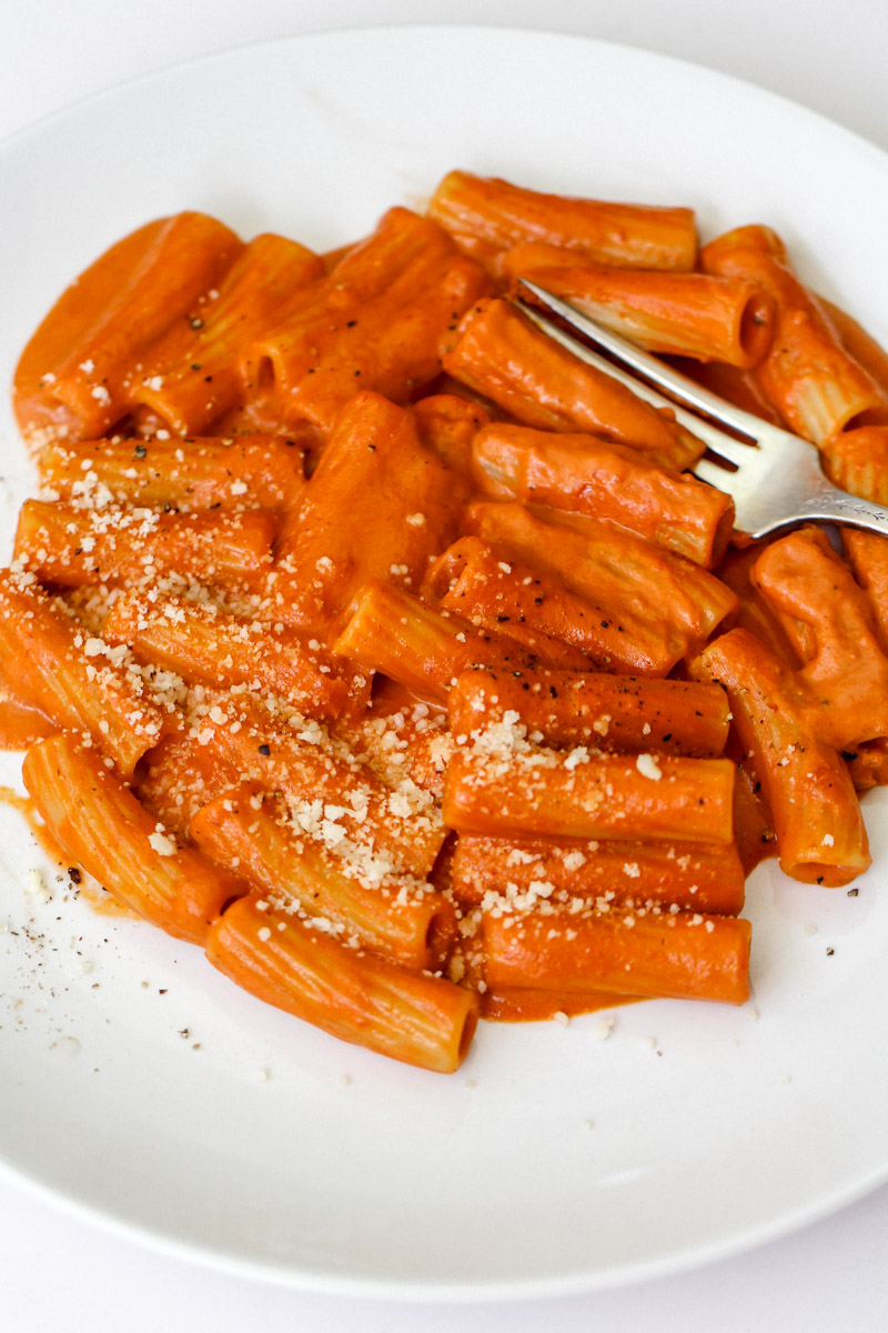 close up image of Italian creamy tomato pasta recipe plated on a white plate with Parmigiano cheese.