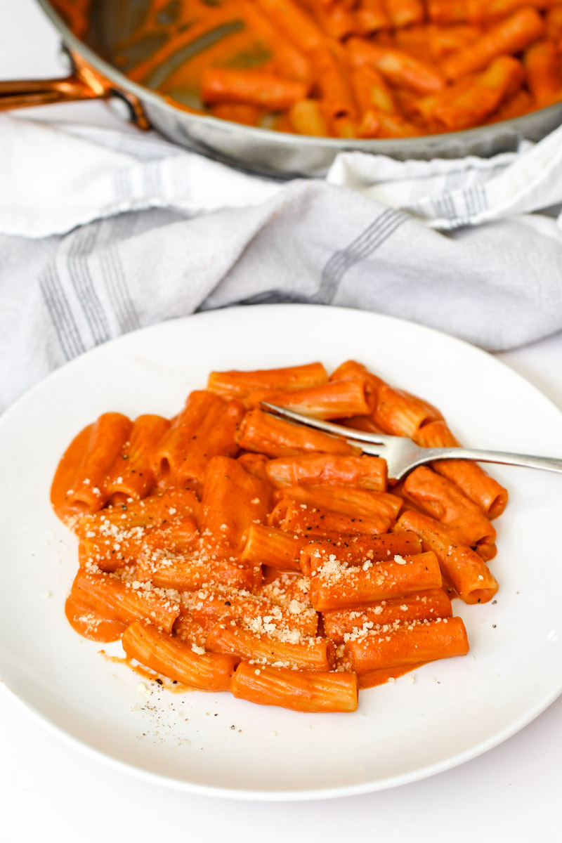 close up image of Italian creamy tomato pasta recipe plated on a white plate with Parmigiano cheese.