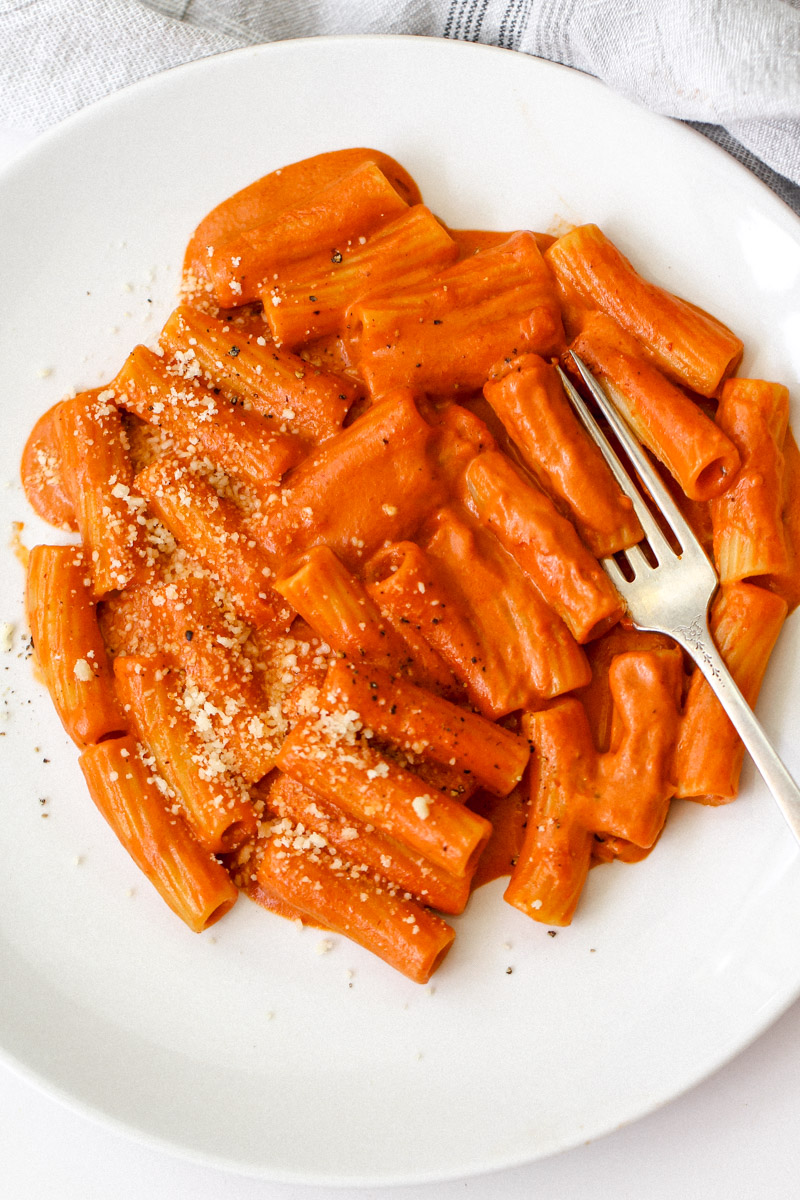 close up image of Italian creamy tomato pasta recipe plated on a white plate with Parmigano Reggiano cheese.