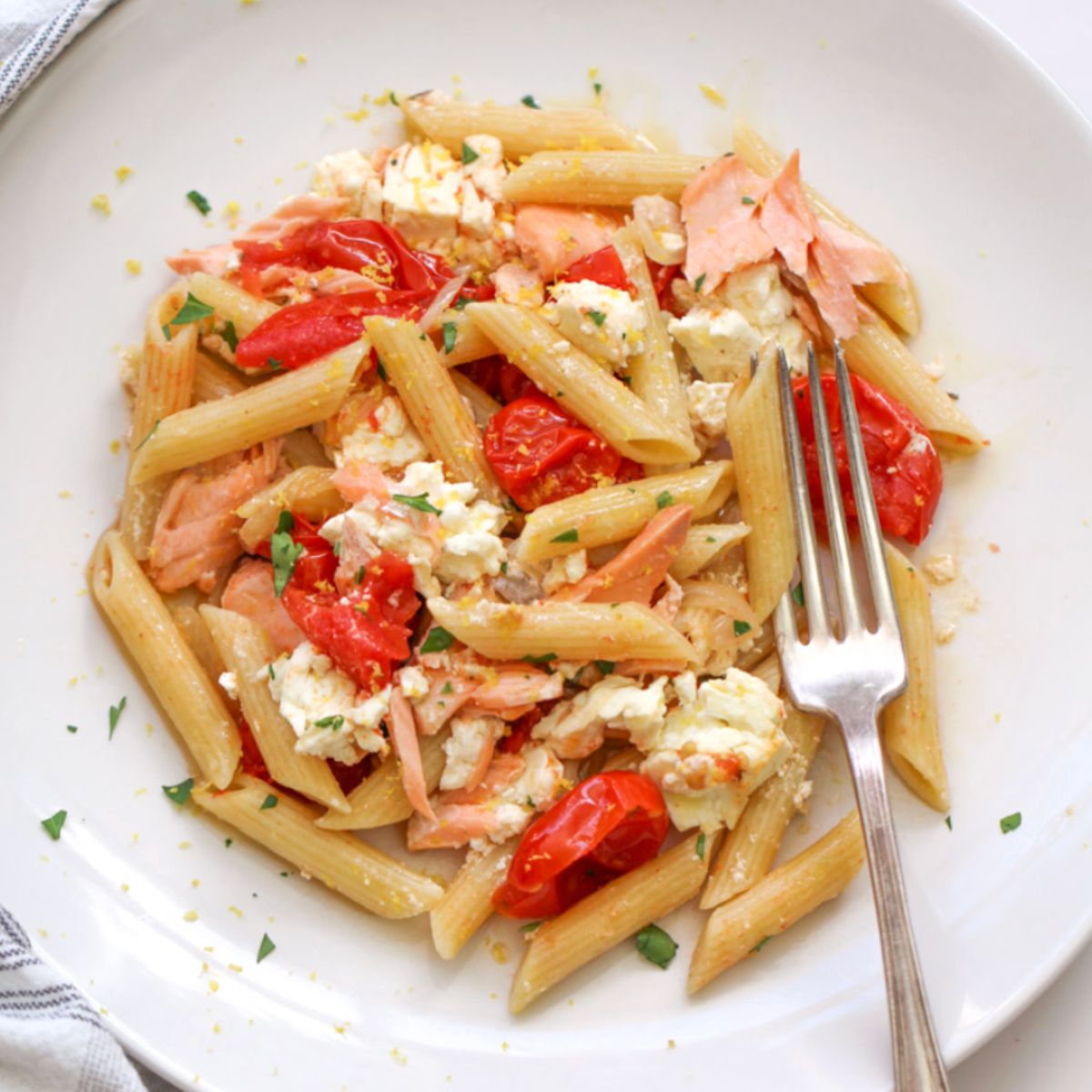 close up image of salmon feta pasta on  white plate with a fork. 
