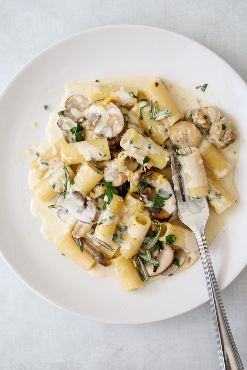 close up image of chicken and mushroom pasta recipe on a white plate with a fork. 