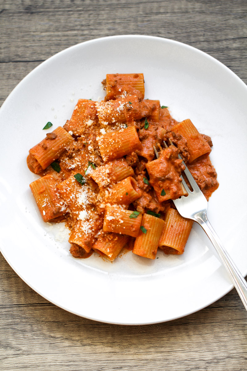 close up image of creamy ground beef tomato pasta on a white plate with a fork.