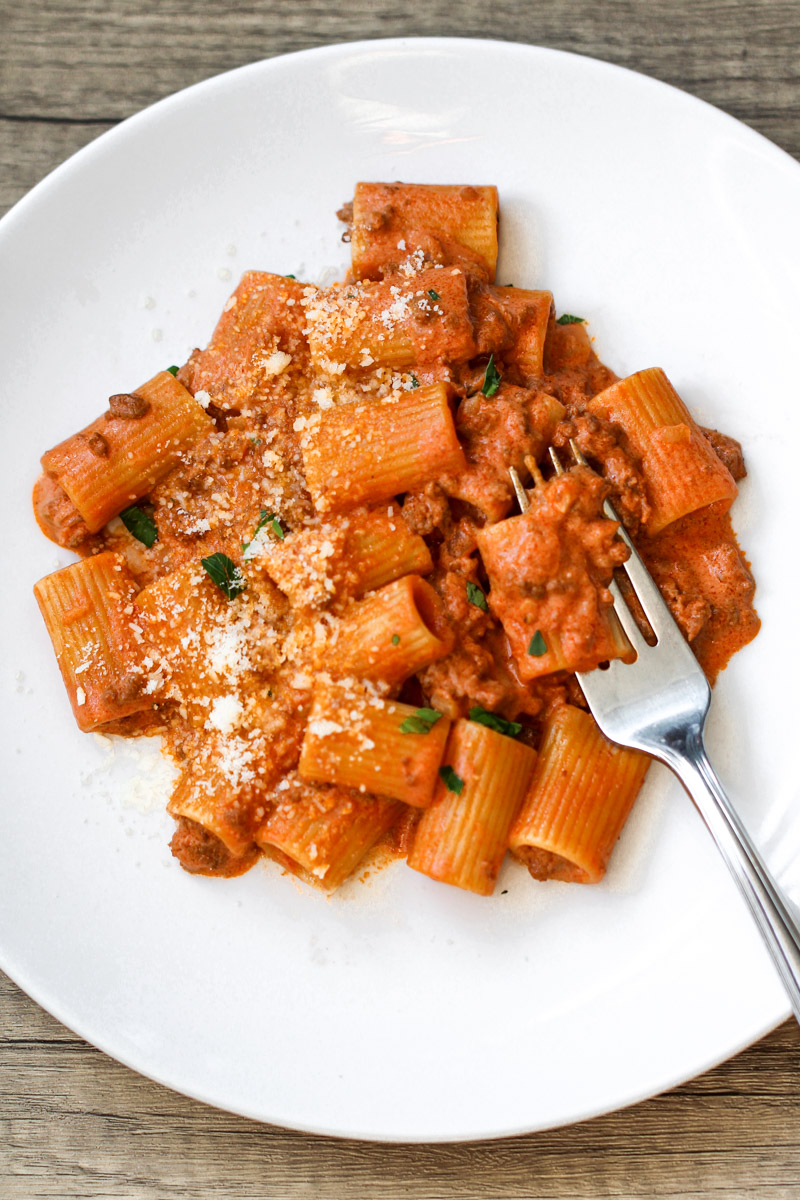 Close up image of pasta with ground beef and creamy tomato sauce on a white plate with a fork.