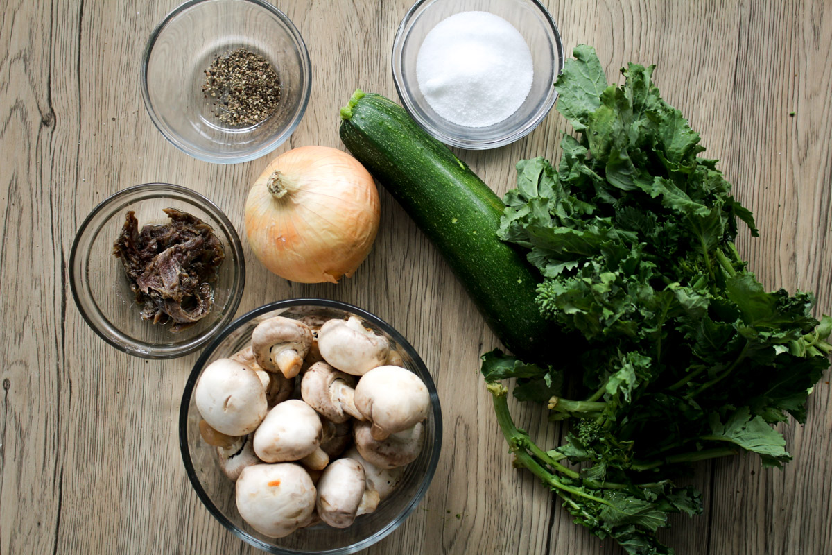 close up image of ingredients to make pasta with mushrooms and zucchini on a wooden background.