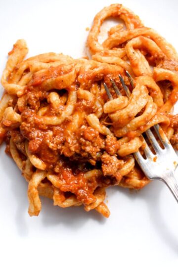 Pici bolognese pasta on white plate.