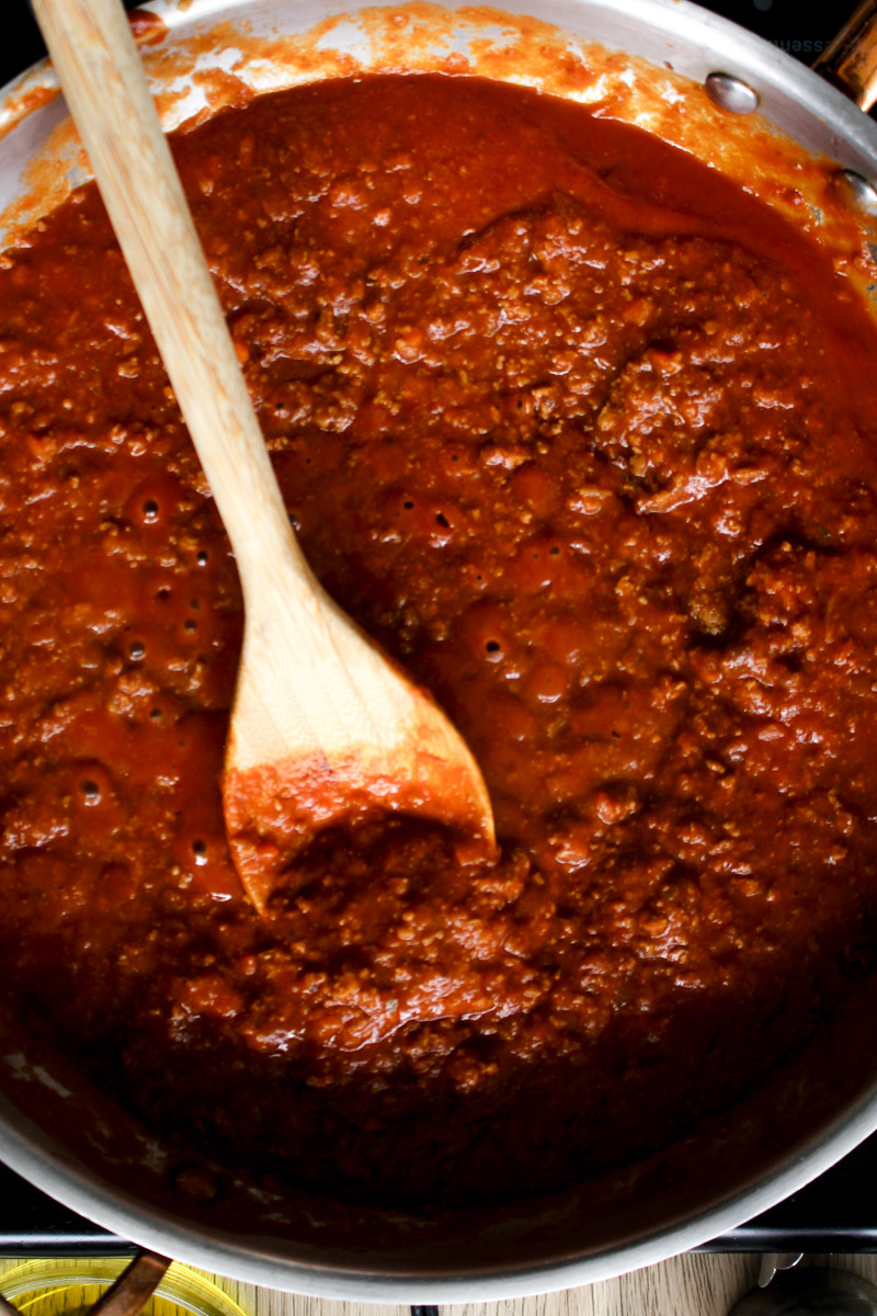 close up image of making Bolognese sauce in a skillet with a wooden spoon. 