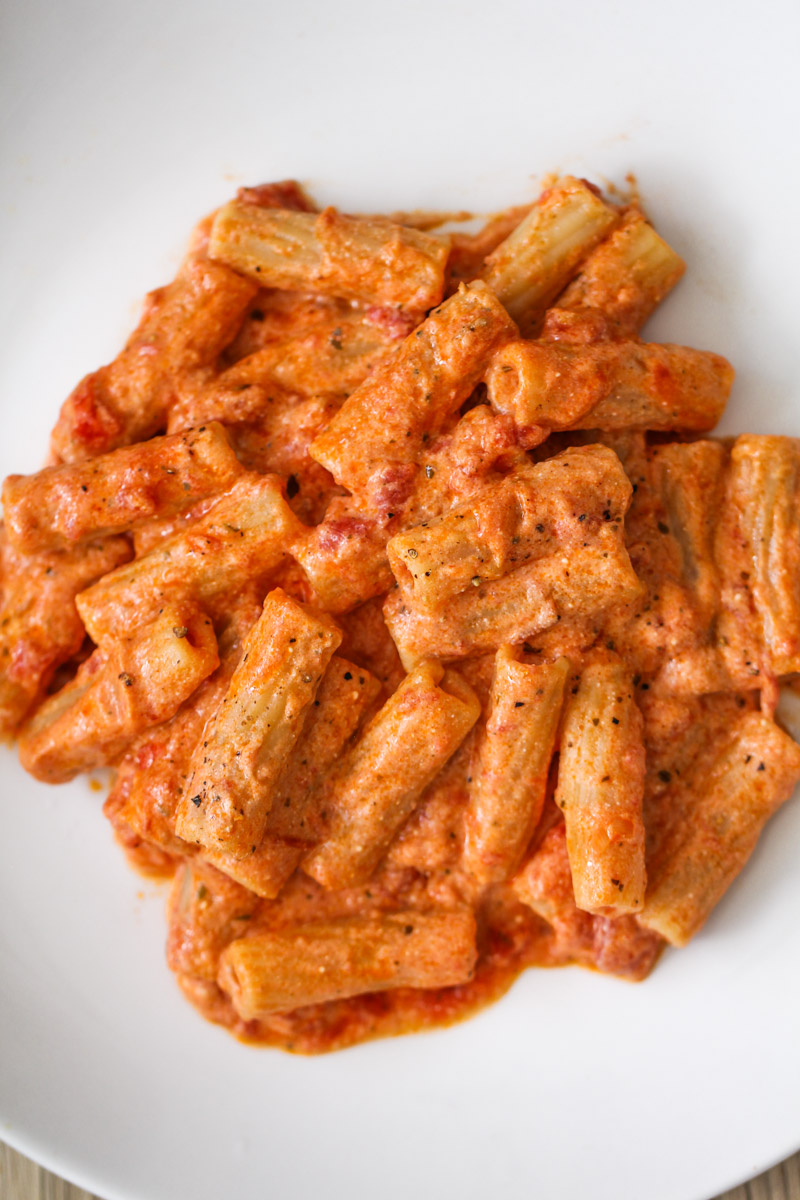 close up image of pasta with tomato ricotta sauce on a white plate. 