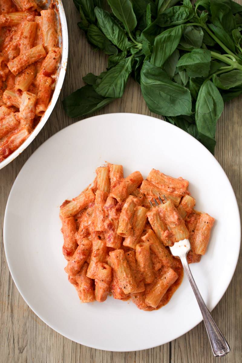 overhead image of tomato and ricotta pasta on a white plate with fresh basil in the background. 