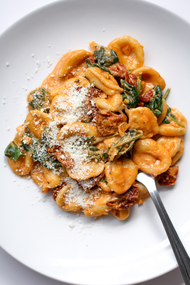 close up image of sun dried tomato pasta on a white plate with a fork. 