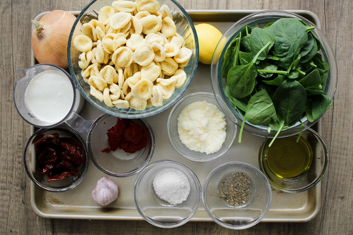 overhead image of ingredients to make sun dried tomato pasta on a baking tray. 