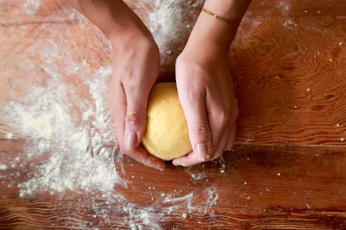 close up image of hands making pasta dough on a wooden board.