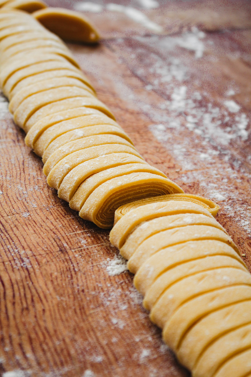 close up image of slicing tagliatelle on a wooden board.