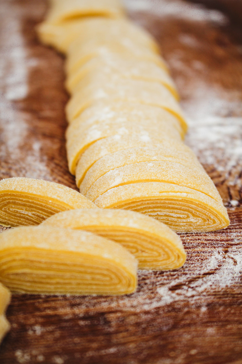 close up image of dough sliced to make tagliatelle pasta on a wooden board.
