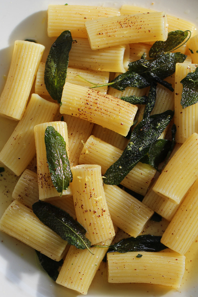 close up image of pasta with a butter and sage sauce on a white plate.