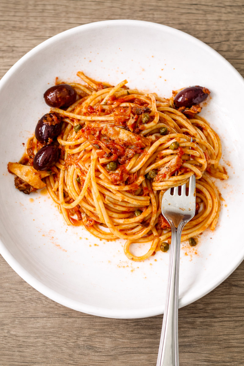 close up image of tuna pasta on a white plate with a fork and a wooden background.