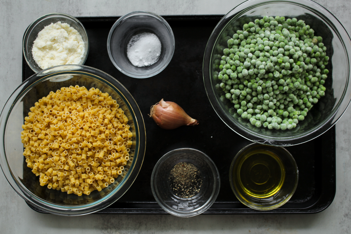 overhead image of ingredients in glass bowls on a baking tray to make pasta and peas. 