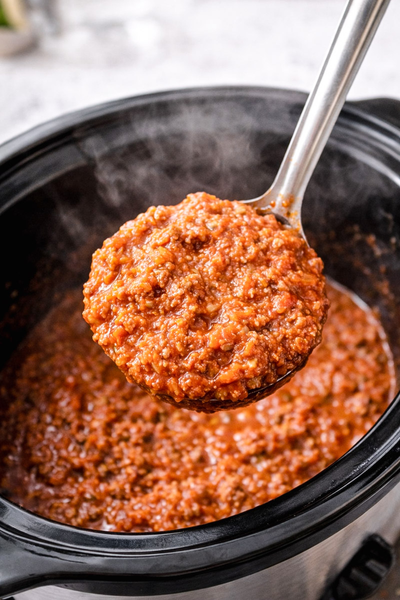 close up image of Bolognese sauce in a slow cooker with a portion on a spoon. 